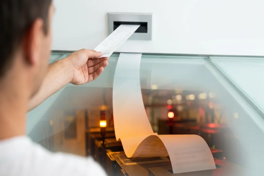 A receipt tape that widens from a narrow strip to a 5x-broad cascade as it passes through a glass floor threshold, embodyi...